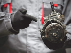 Auto mechanic showing a broken air conditioning compressor close up.