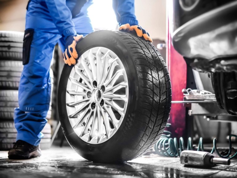 Auto mechanic working in garage and changing wheel alloy tire.