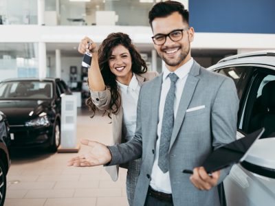 Happy and beautiful middle age business woman buying new car at showroom. A nice seller helps her make the right decision.