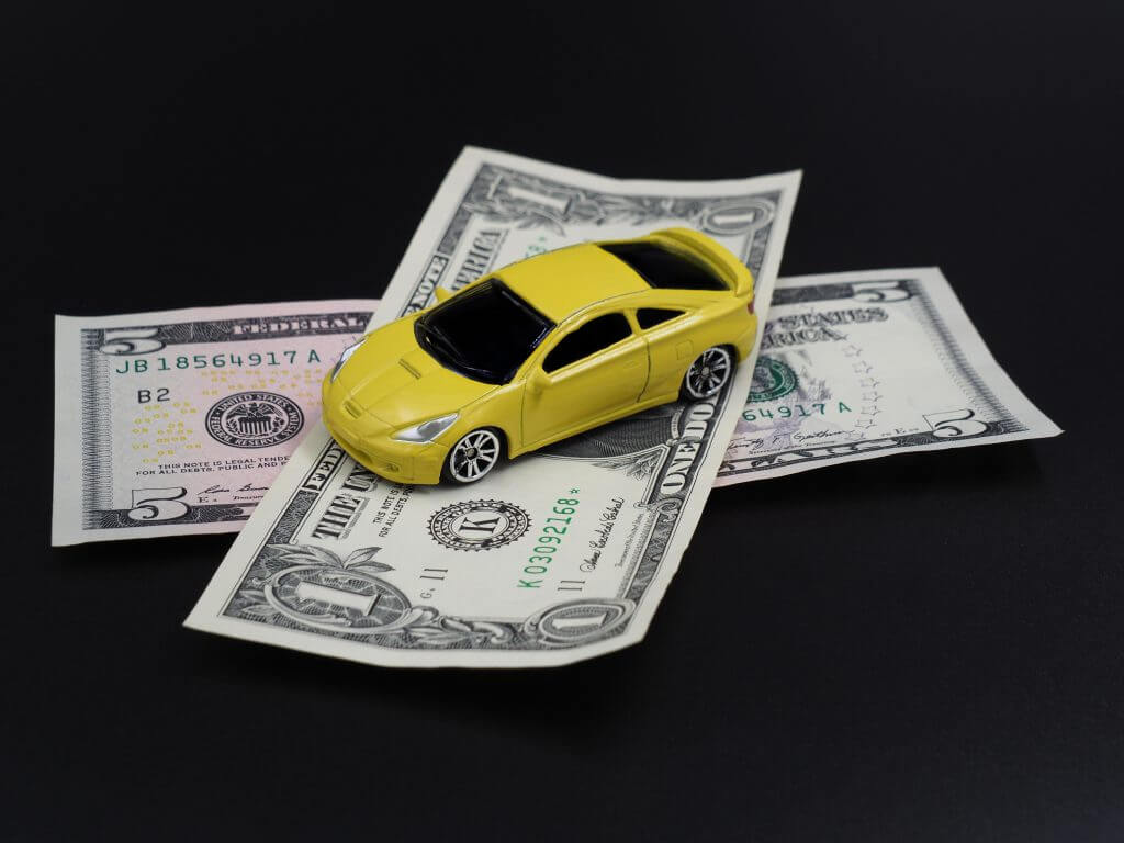 Yellow toy car on dollar bills on a black gradient background. Collapse of prices, discount on the car.