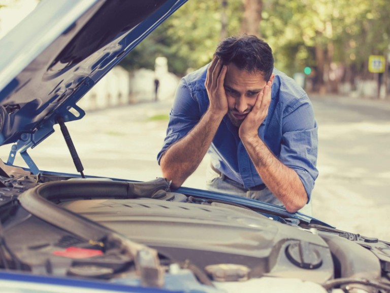 young stressed man having trouble with his broken car looking in frustration at failed engine