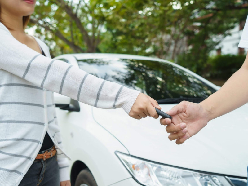 Young women giving a key car to young man in font of car