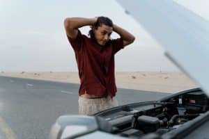 Man standing in front of car with hands on his head out of frustration