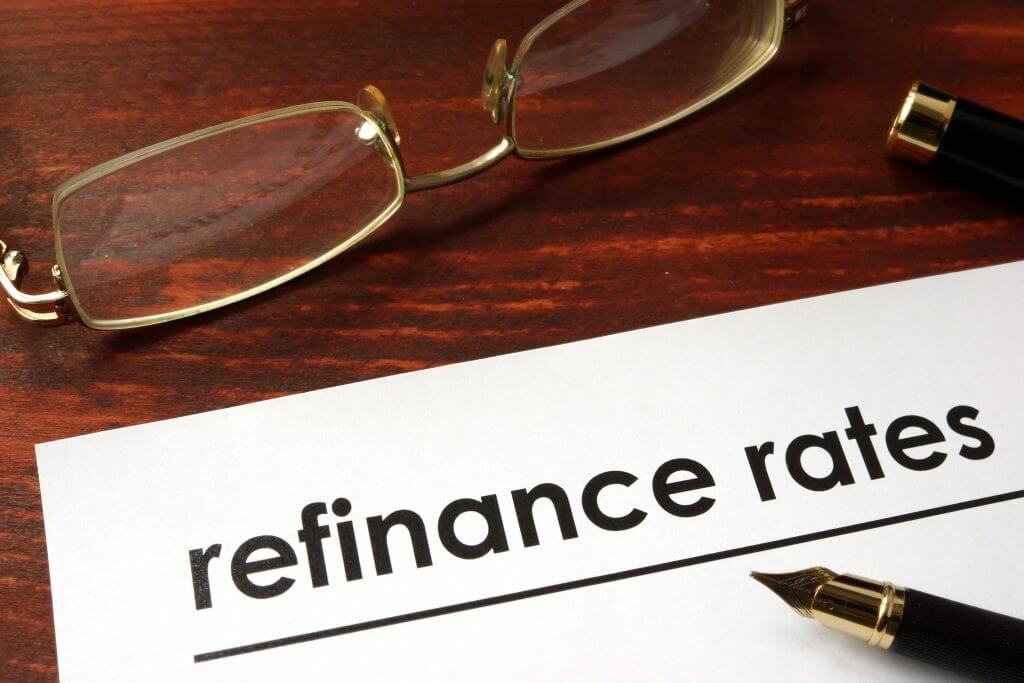 Paper with words refinance rates on a wooden background.