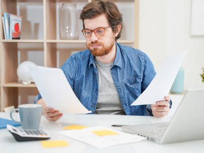 Young troubled guy calculating bills tax expenses and counting home business