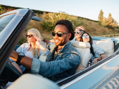 Group of happy young friends driving car in summer