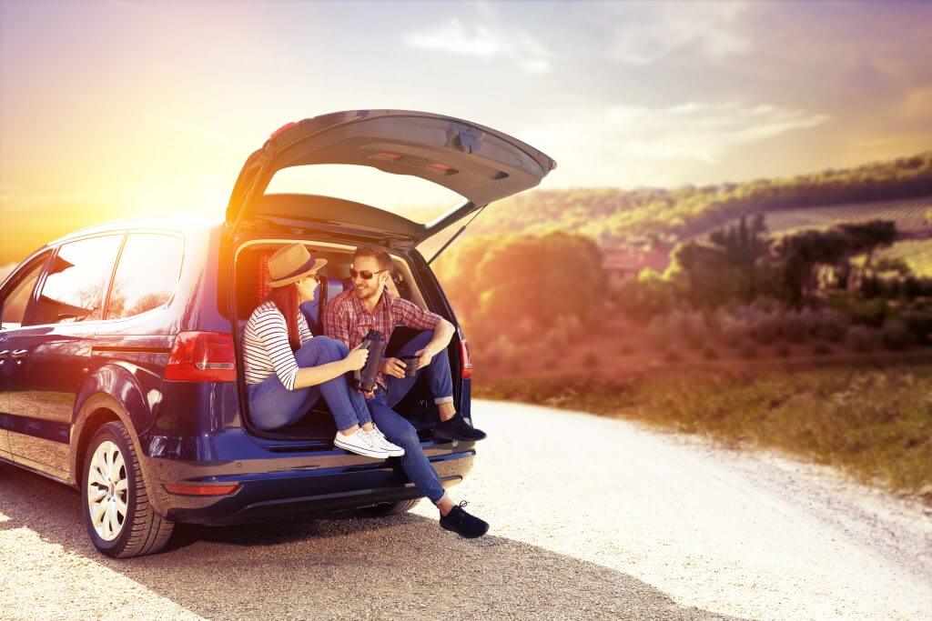 couple sitting and talking at the trunk of a car parked at the side of the road