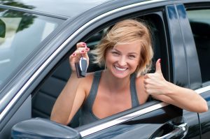 Young happy woman showing the key of new car. Woman driver holding car keys.