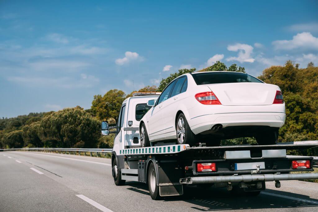 A white car being towed on a flat bed down a highway