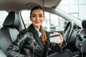 Woman holding credit card and smiling at camera in car