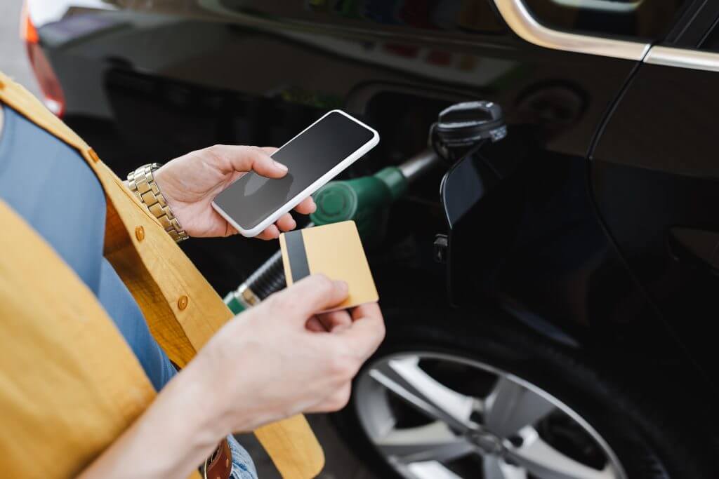 Cropped view of woman holding smartphone and credit card while refueling car on gas station