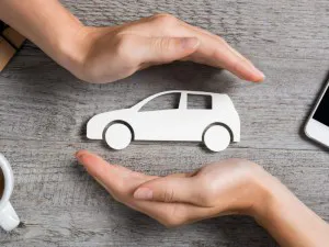 Hands protecting icon of car over wooden table. Top view of hands showing gesture of protecting car. Car insurance and automotive business concept.