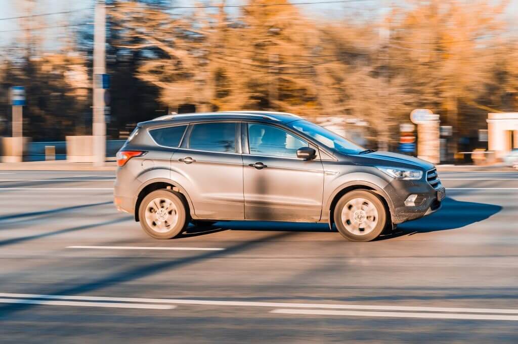 UV car in motion. Ford Escape third generation moving on the street. Gray Ford Kuga is driving on urban highway with autumn blurred background