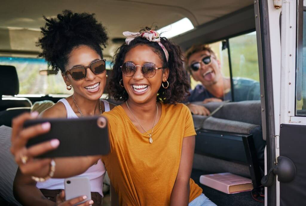 Travel, smile and selfie with friends on road trip in car for adventure, summer and freedom on California holiday. Happy, support and mobile with group of people with phone for social media together.