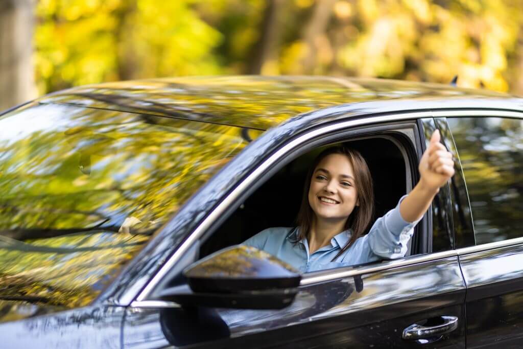 Happy woman inside a car driving in the street and gesturing thumb up
