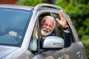 Happy senior man waving hand through window of gray car