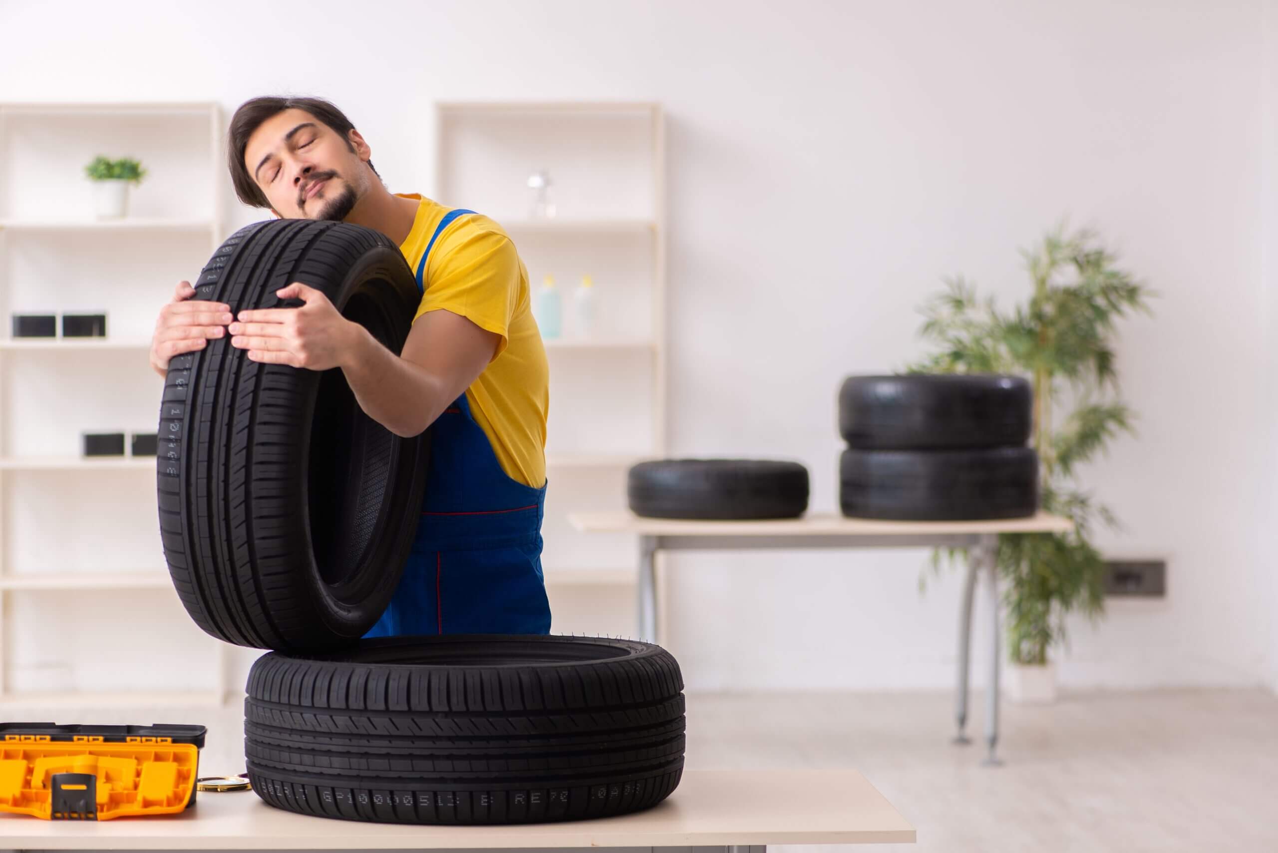 Young garage worker with tyre at workshop