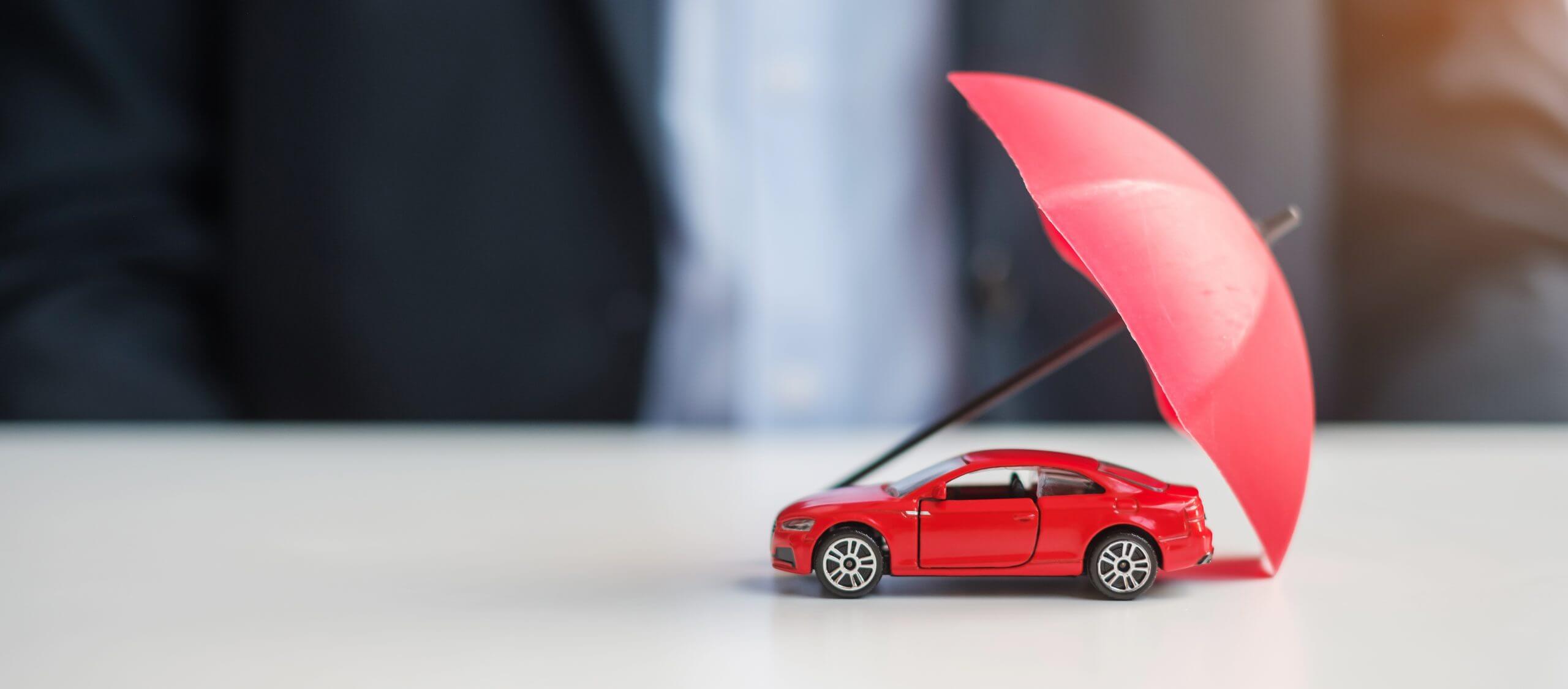 Businessman hand holding umbrella and cover  red car toy on table. Car insurance, warranty, repair, Financial, banking and money concept