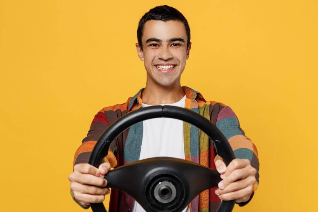 Young smiling fun middle eastern man 20s he wear casual shirt white t-shirt pretending driving hold in hand steering wheel isolated on plain yellow background studio portrait People lifestyle concept