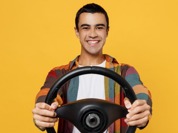 Young smiling fun middle eastern man 20s he wear casual shirt white t-shirt pretending driving hold in hand steering wheel isolated on plain yellow background studio portrait People lifestyle concept
