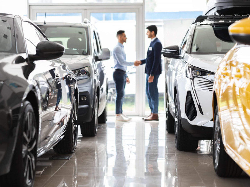 Customer and sales assistant shaking hands, car showroom interior