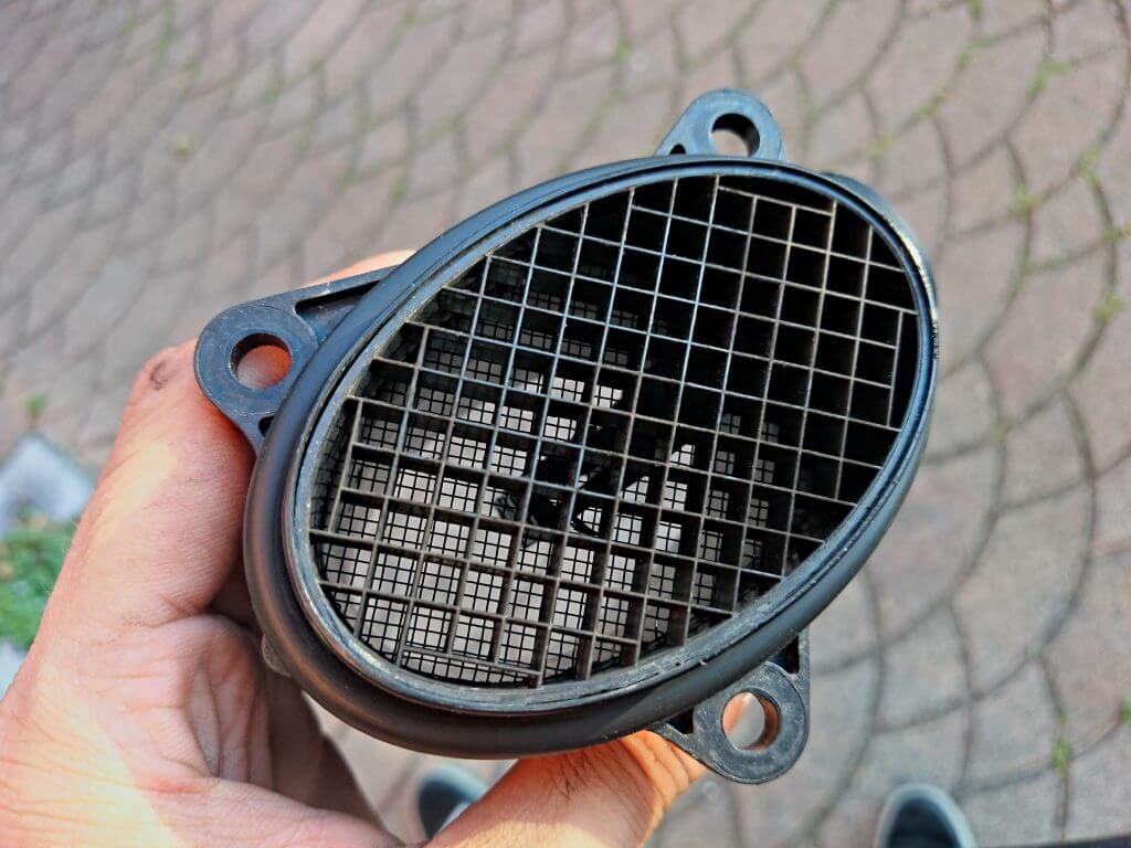 up close photo of a mass air flow sensor held by a person's hand