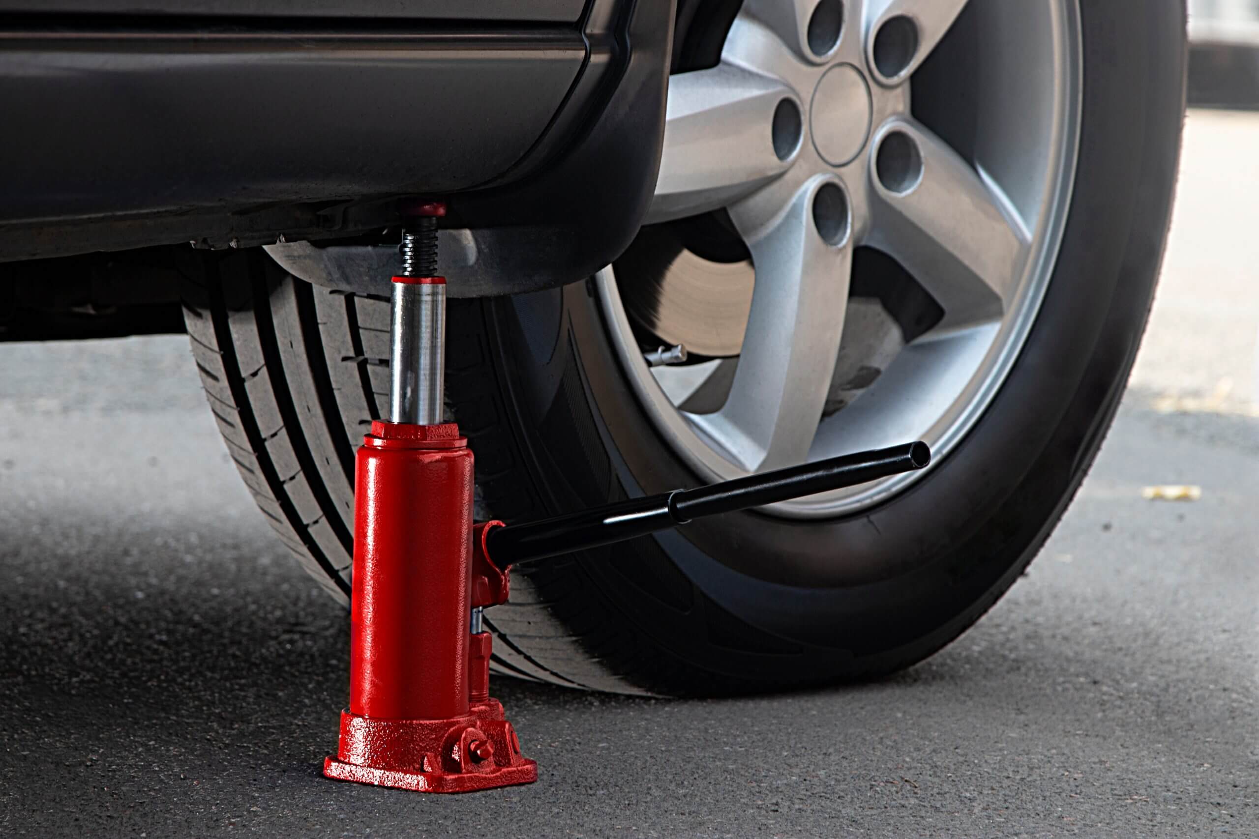 The red hydraulic bottle jack is installed under the machine and lifting it. Bottle jack near car wheel