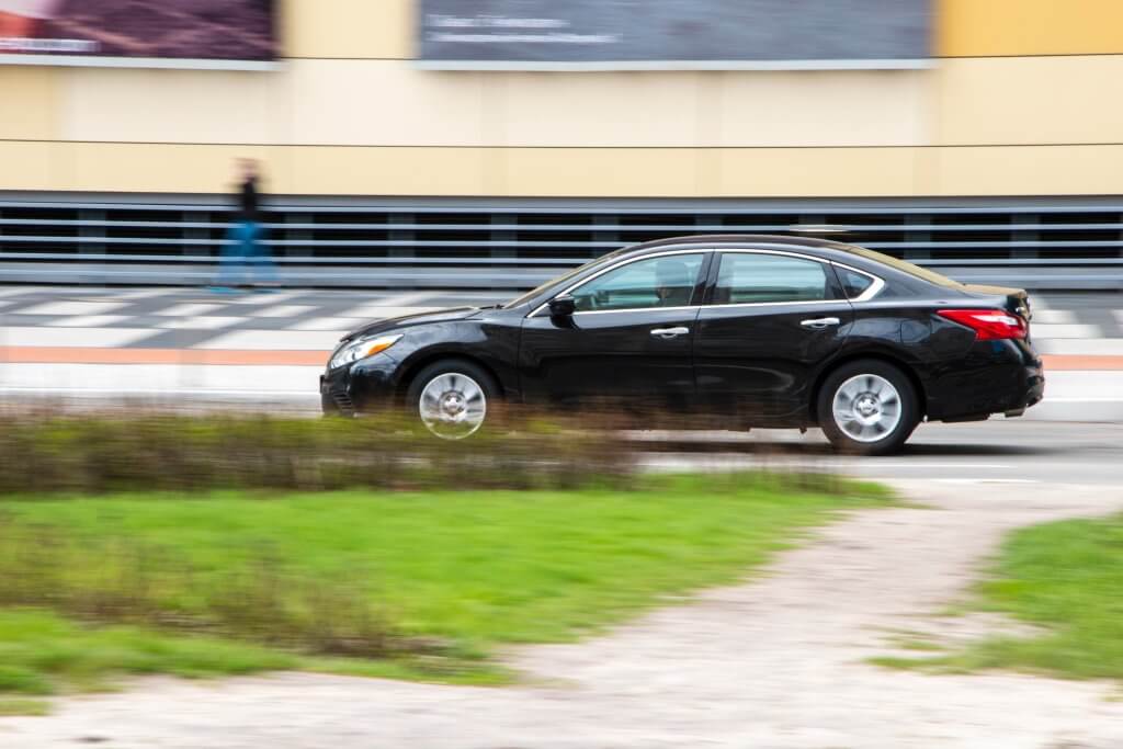 Black Nissan Altima car moving on the street. Editorial