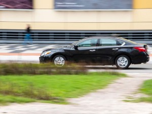 Black Nissan Altima car moving on the street. Editorial