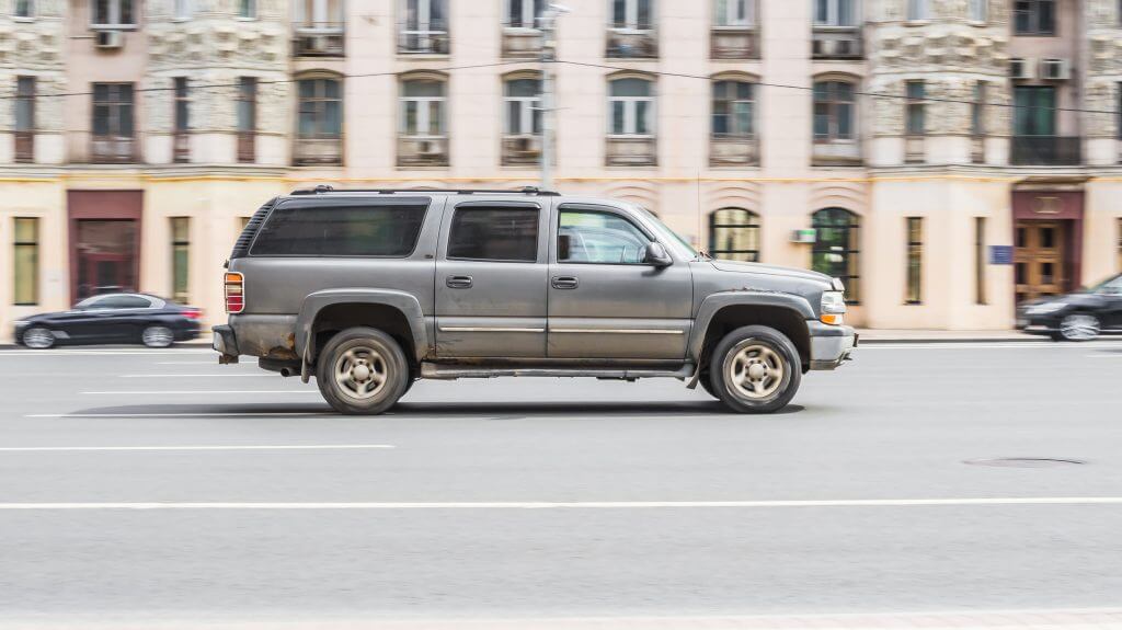 Old gray rusty Chevrolet Tahoe GMT800 in motion on a city street. Old GMC Yukon 5-door SUV side view on city highway