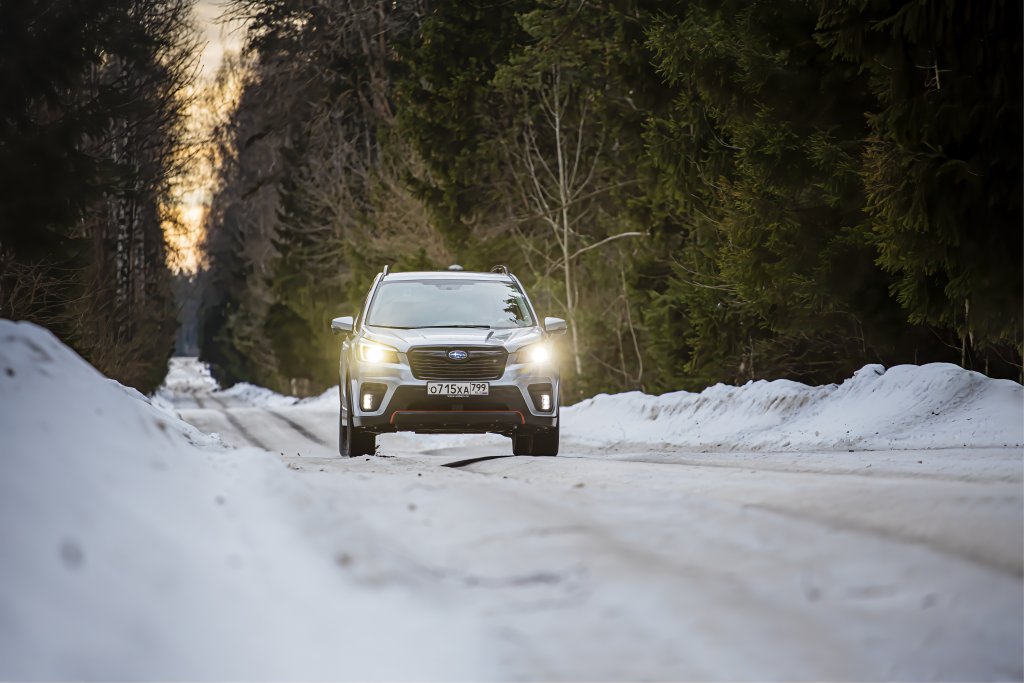 Silver Subaru Forester drives through the forest on a snowy road in winter