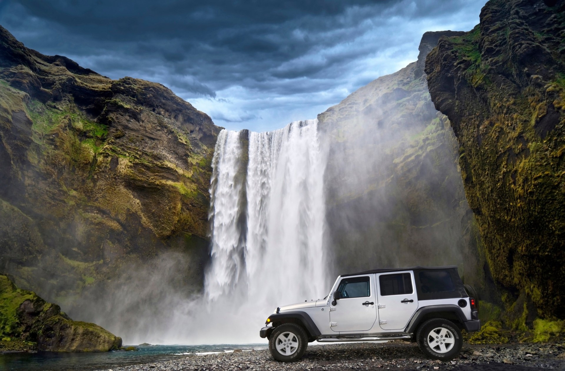 White Jeep Wrangler parked beneath a waterfall