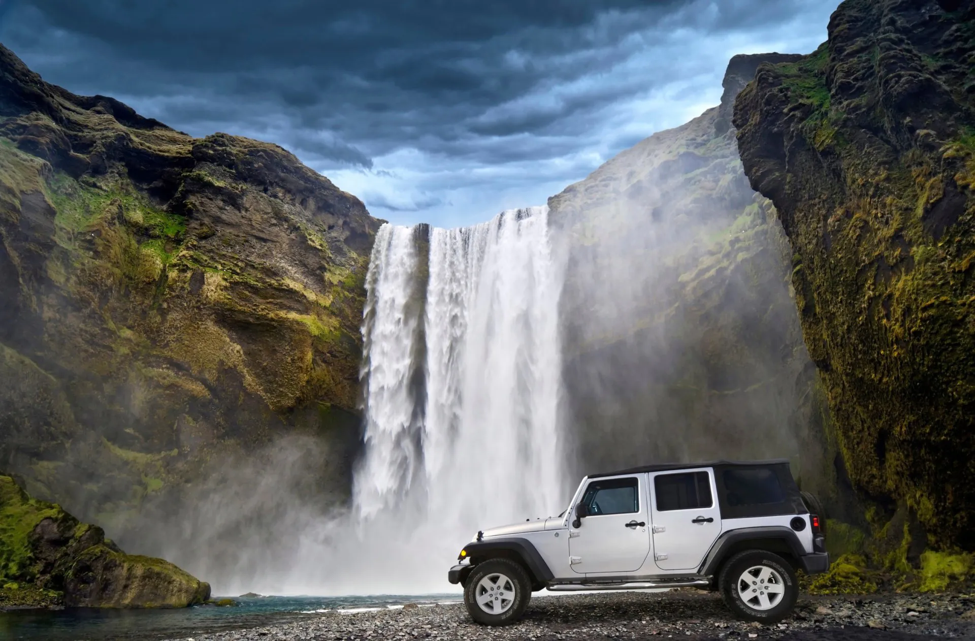 White Jeep Wrangler parked beneath a waterfall