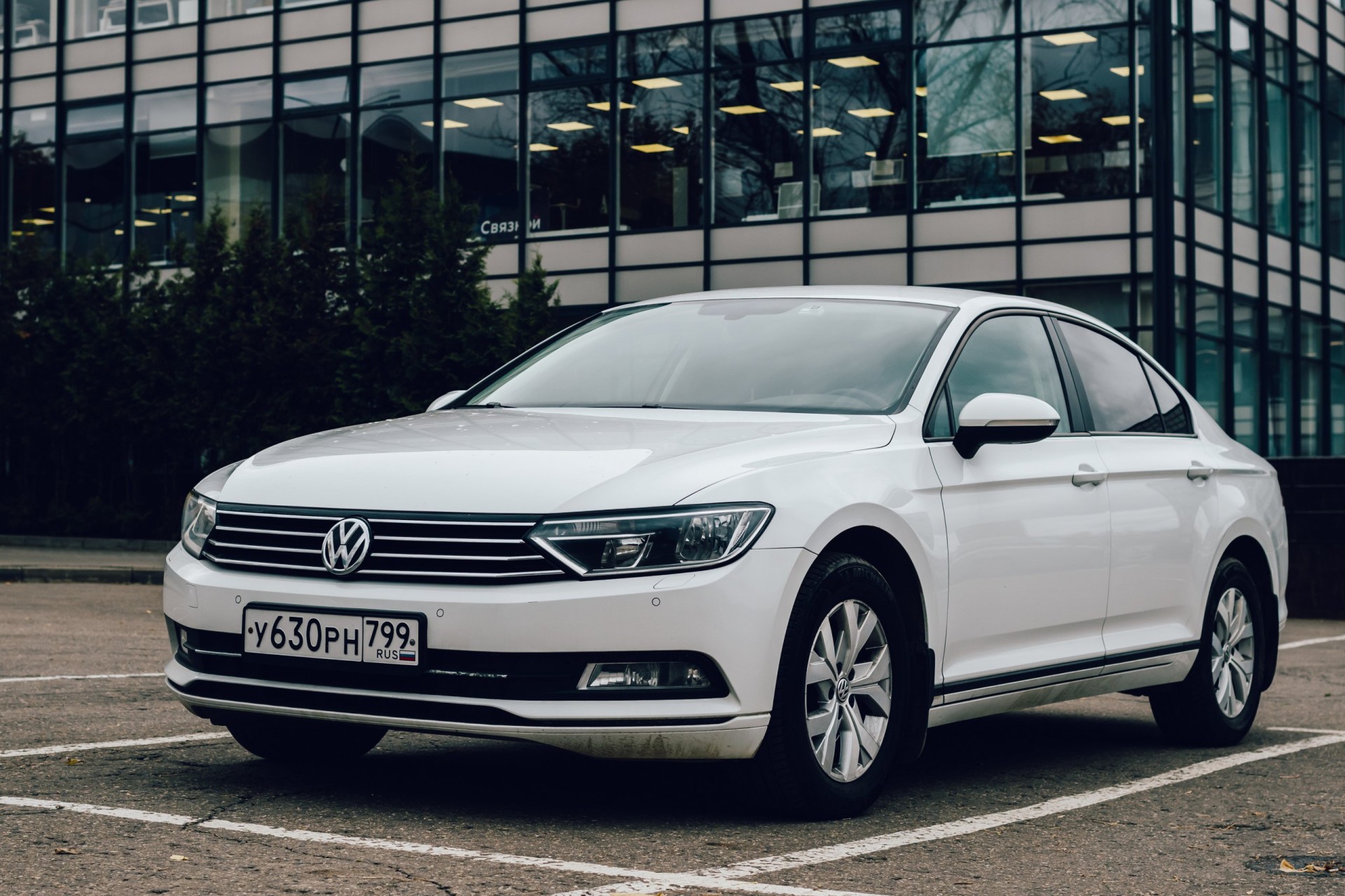 2017 White car Volkswagen Passat B8 is parked on the parking in front of glass office building