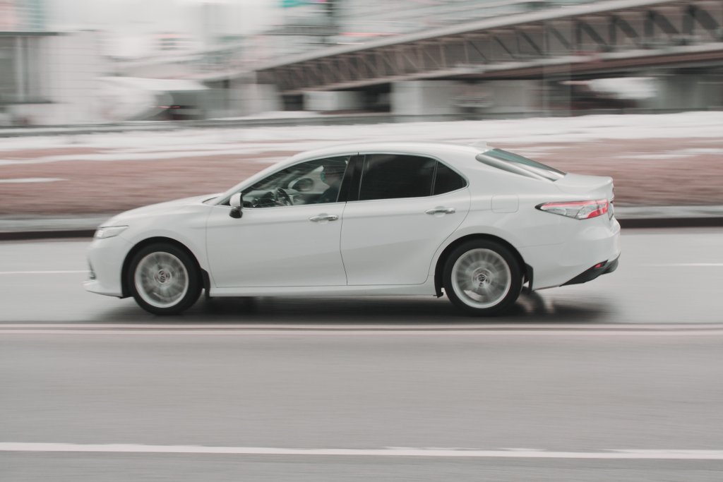 2015 Toyota Camry rides on the road. A white sedan car rushes along the street