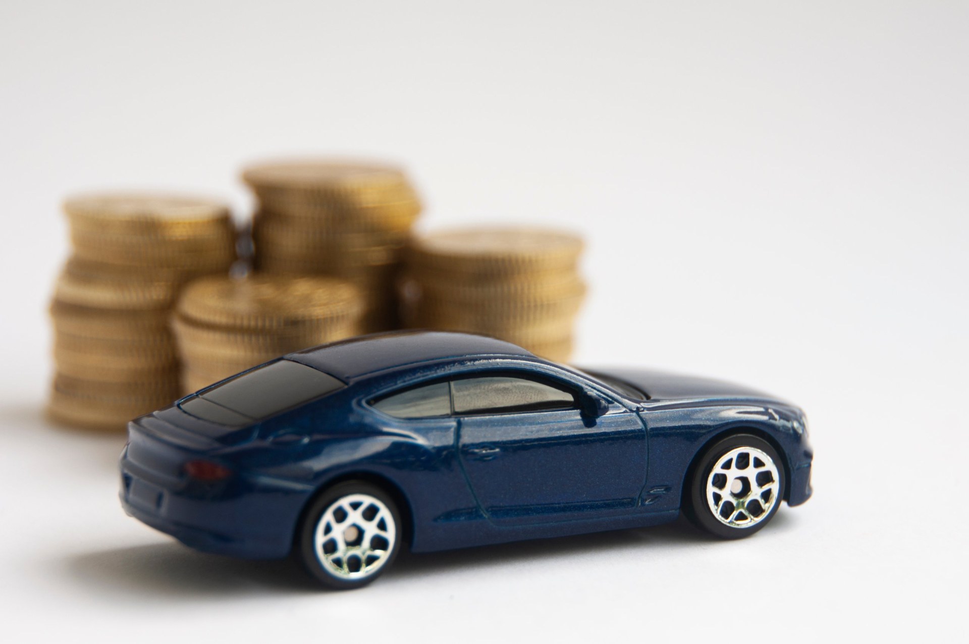 Miniature toy car of Bentley Continental GT with gold coin background.