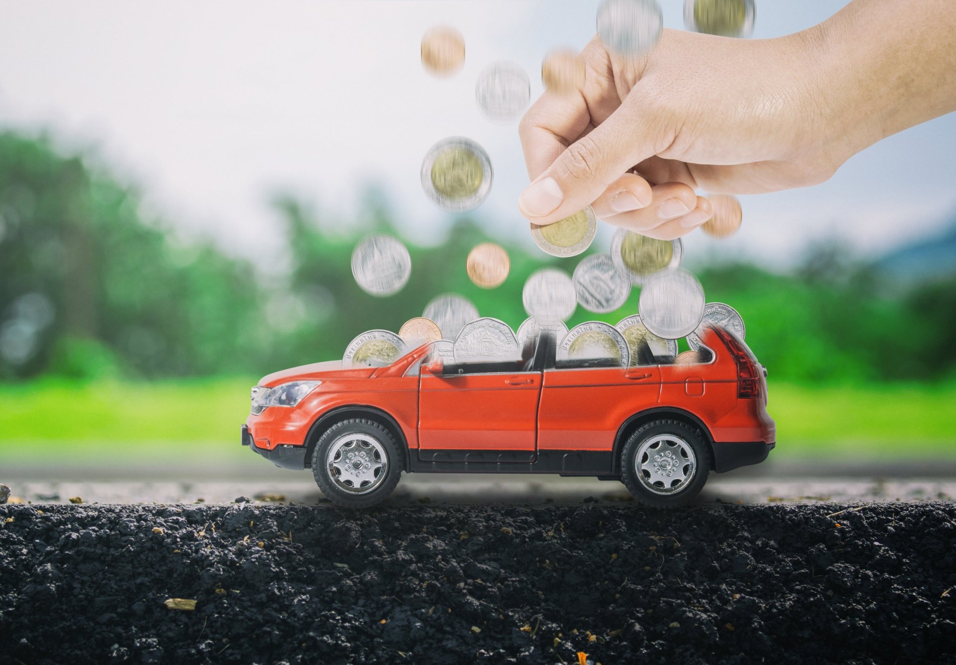 a hand putting coins into a red car to fill up. The concept of saving to buy the new car.