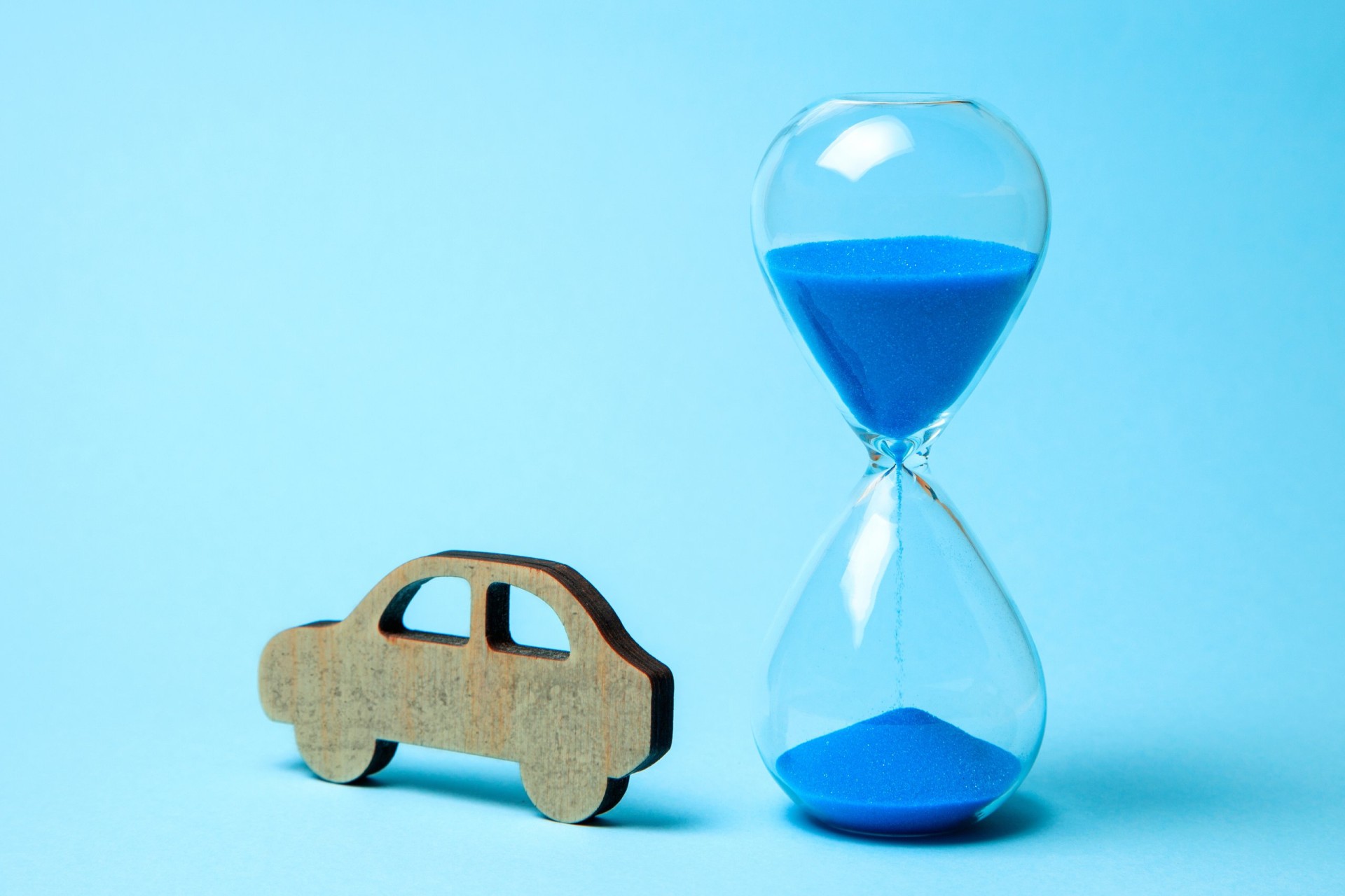 Depreciation or depreciation of the car over time. Wooden car and hourglass on blue background. 
