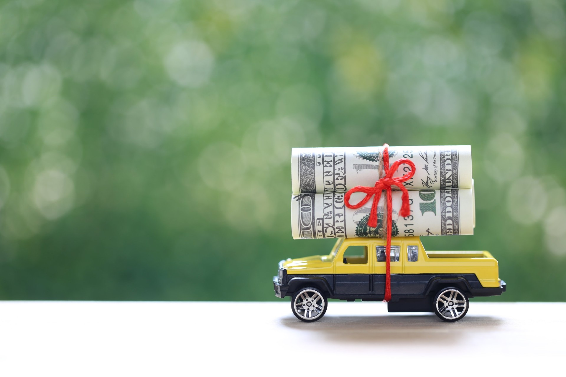 Miniature car and banknotes on nature green background, 