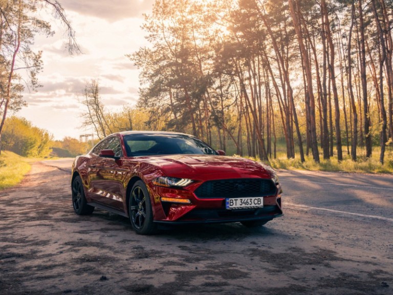 American muscle car Ford Mustang in a red color on the forest road..