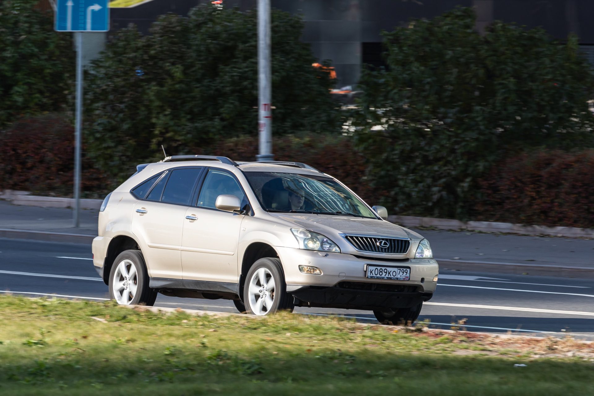 beige 2003 Lexus RX300 is driving fast on the street on a warm autumn day against the backdrop of a park