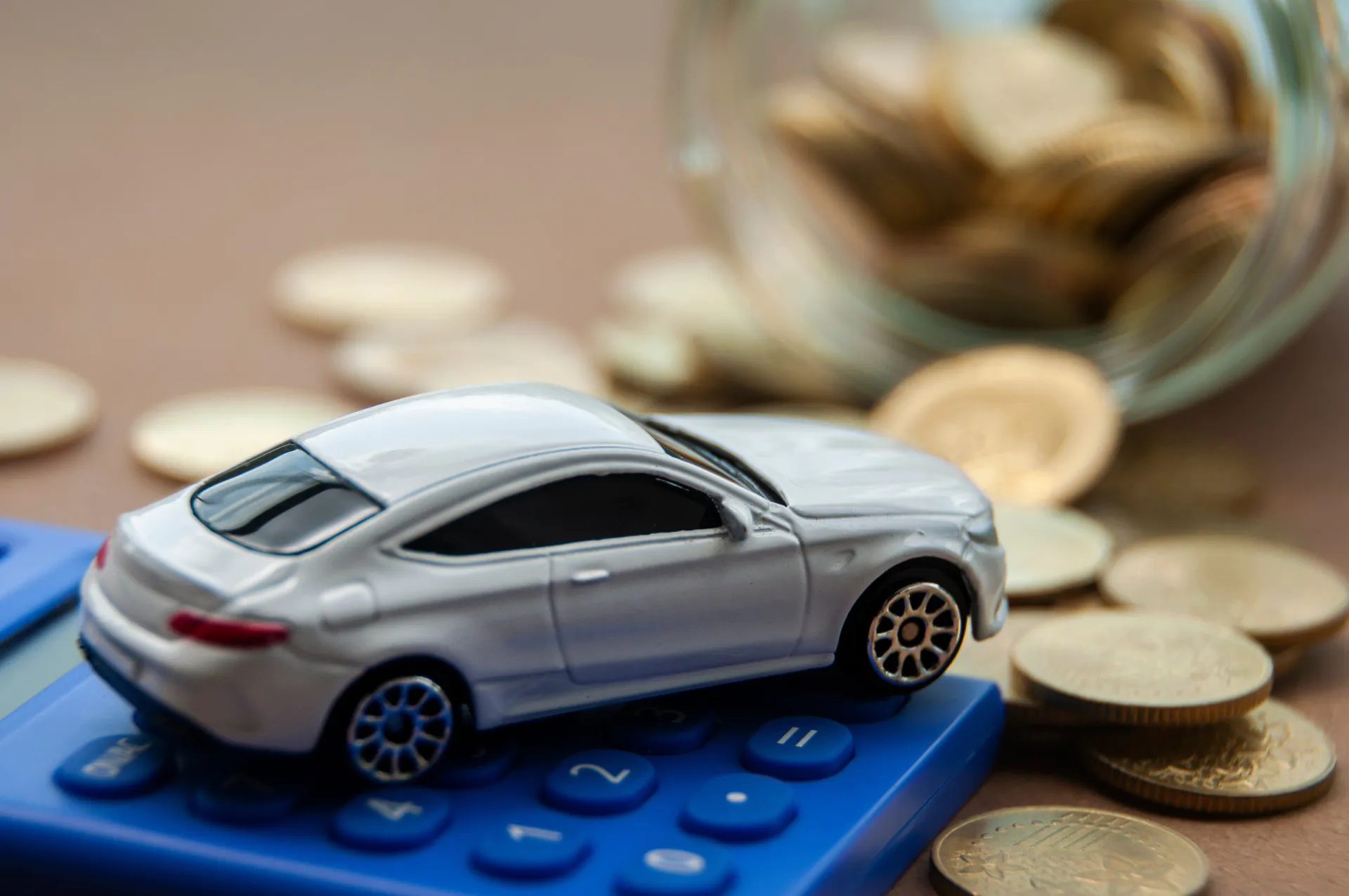 Miniature toy car of Mercedes AMG on top of calculator with gold coin background.