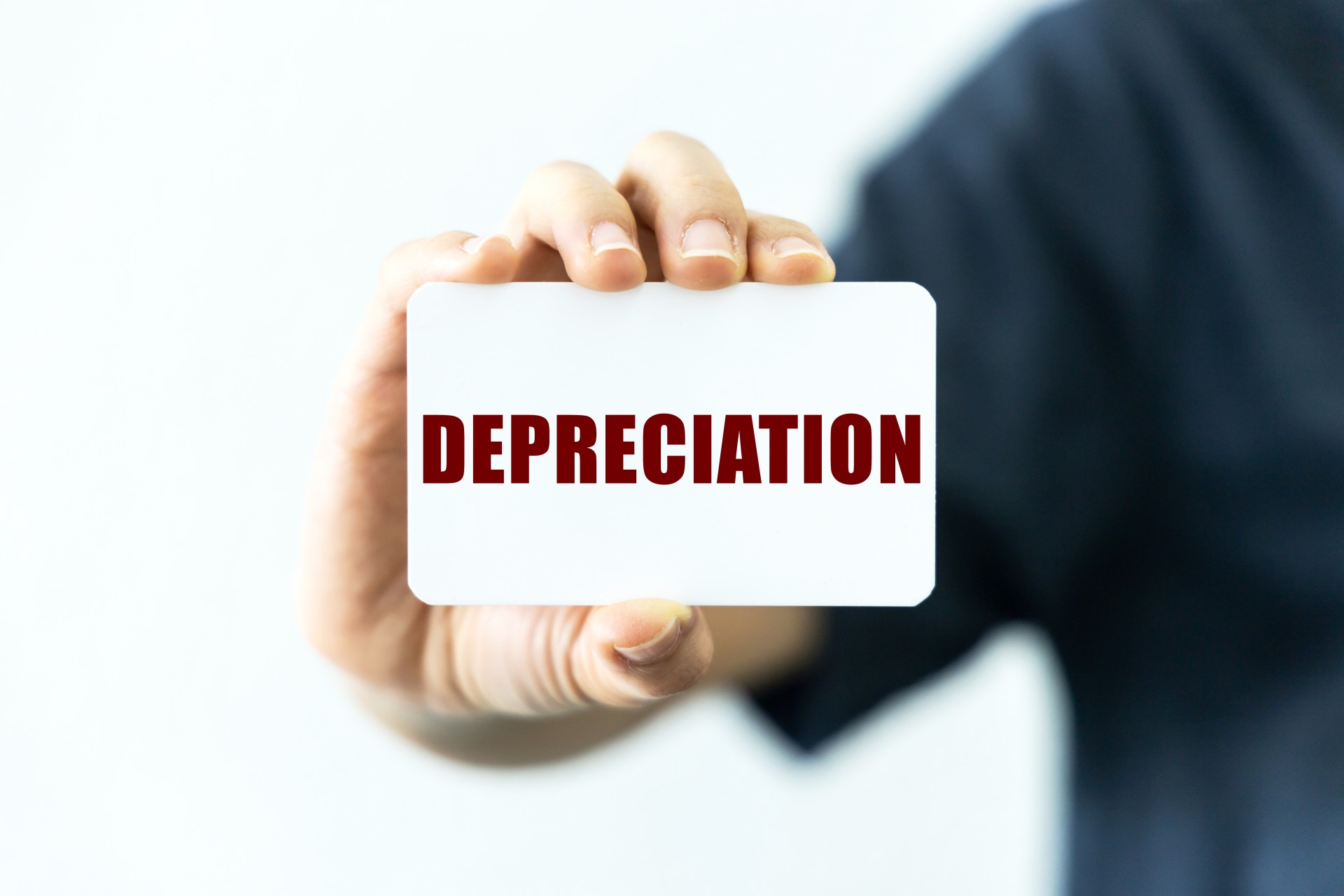 Depreciation text on blank business card being held by a woman's hand with blurred background. Business concept about Depreciation.