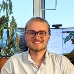 Nicholas Holt sitting in front of his computer monitor smiling